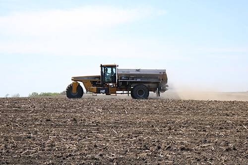 A yellow tractor driving through a field dispensing fertilizer to help crops grow