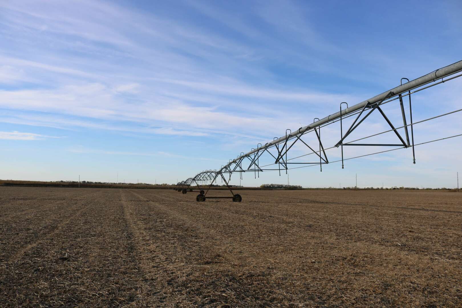 A view of a large farming irrigation system in the middle of a dry brown field with blue skies overhead